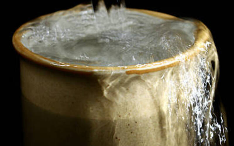 Cup of water that is overflowing, isolated on black background.